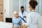 Elderly woman sitting on a hospital bed with two young doctors with clipboard and x-ray photo standing