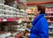 An elderly woman is standing by the shelves with chicken eggs in the grocery store