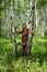 Elderly woman stands at the birch and looks up.