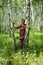 Elderly woman stands among the birches in a summer forest.