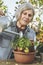 Elderly woman waters plant in pot on sunny day