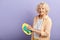 Elderly woman wiping plate and looking at the camera isolated on violet.