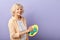 Elderly woman wiping plate and looking at the camera  on violet.