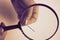 An elderly woman with wrinkled fingers holds a magnifying glass and through the transparent glass is visible a steel