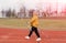 An elderly woman in a yellow sports jacket practices Nordic walking outdoors on the stadium`s rubber treadmill. A sunny sunset.