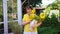 An elderly woman in a yellow top with a bunch of sunflowers in a watering can.