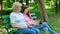 Elderly woman and young woman sitting on the bench in the park and making a video call via computer tablet. Adult Mother