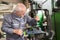 Elderly worker watches processing detail on milling machine