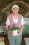 Elderly wrinkled woman is holding a white pot with a homemade violet flower in her hands. Home breeding of flowers. concept is