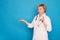 Eldery caucasian doctor lady in white coat and with stethoscope on blue background. Emotional portraits: she showing something in