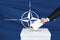 Election in Nato. The hand of man putting his vote in the ballot box. Waved Nato flag on background.