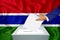 Elections in the country - voting at the ballot box. A man`s hand puts his vote into the ballot box. Flag Gambia on background