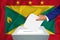 Elections in the country - voting at the ballot box. A man`s hand puts his vote into the ballot box. Flag Grenada on background