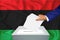 Elections in the country - voting at the ballot box. A man`s hand puts his vote into the ballot box. Flag Libya on background