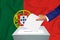 Elections in the country - voting at the ballot box. A man`s hand puts his vote into the ballot box. Flag Portuguese on backgroun