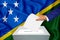 Elections in the country - voting at the ballot box. A man`s hand puts his vote into the ballot box. Flag Solomon Islands on