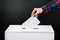 Elections and voting concept. Woman puts ballot paper in box on a black background