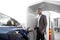 Electric cars, EV concept, eco friendly fuel. Portrait of young smiling black man in business clothes, recharging his