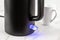 Electric kettle switch glows blue while turned on. Matte black kettle for heating water to boiling for tea and coffee. Modern