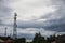 Electric pillar over trees and house roofs, grey cloudy sky panorama. Skyline with communication towers