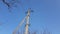 Electric pillar with wires and bare tree branches in blue sky.