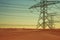 Electric power lines and electricity transmission pylons in desert at sunset