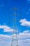 Electric power transmission. Power line pole - high-power electrical transmission tower - against the blue sky and white billowing