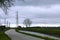 Electric pylon, tree and house along the river and the road in the countryside on a rainy day.