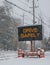 Electric road traffic mobile sign by the side of a snow covered road with snow falling that says, Drive Safely.
