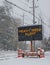 Electric road traffic mobile sign by the side of a snow covered road with snow falling warning of heavy snow alert