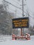 Electric road traffic mobile sign by the side of a snow covered road with snow falling warning of heavy snow alert