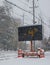 Electric road traffic mobile sign by the side of a snow covered road in winter with snow falling indicating that the temperature