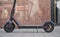 Electric scooter parked on tiled pavement - closeup detail, marble wall and glass door background
