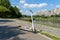 An electric white scooter stands on the bandwagon on the street. City park along the promenade. Sunny summer day.