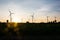 Electric wind turbines farm silhouettes on sun background