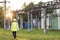 Electrical engineer wearing a helmet and safety vest walking near high voltage electrical lines towards power station