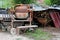 Electrical metal concrete mixer covered with rust next to rusted wheelbarrow construction cart surrounded with construction