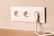 Electrical outlets with plug on beige wall