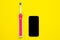 Electrical tooth brush of round shape and modern black mobile phone lying on bright yellow background