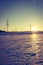 Electrical tower on a snowy field. Sun goes down, orange colors, evening scenery