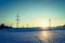 Electrical tower on a snowy field. Sun goes down, orange colors, evening scenery