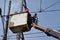 Electrical Workers On Telehandler With Bucket installing High tension wires on tall concrete post. Underside view low angle