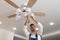 Electrician changing light bulb in ceiling fan indoors