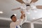 Electrician changing light bulb in ceiling fan indoors