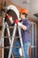 Electrician in hardhat standing stepladder and repairing lamp on