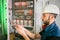 An electrician in a helmet connects the wires of the circuit breakers in the electrical box.  A qualified engineer works in an