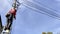 Electrician in helmet fixes wires on ladder near high pole