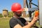 Electrician in red helmet with multimeter on electric pole