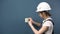 An electrician repairs an outlet in the house. A woman in special clothing and a helmet installs an outlet.