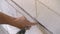 Electrician securing cables in groove or chase on a wall in newly built house, using power drill and screws - closeup detail